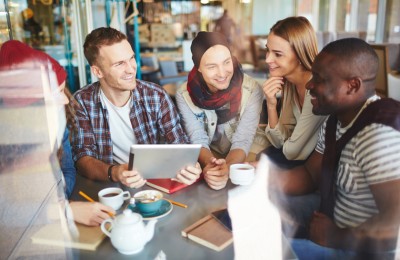 Community group of people chatting around a table and looking up information on a tablet device
