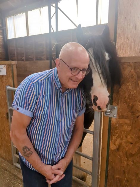 Photo of Andy stood next to a horse in a stable, laughing.