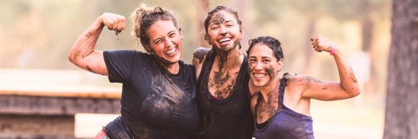 Tough Muddler - image shows three young women covered in mud and smiling and flexing muscles, after having completed an obstacle course