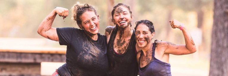 Tough Muddler - image shows three young women covered in mud and smiling and flexing muscles, after having completed an obstacle course